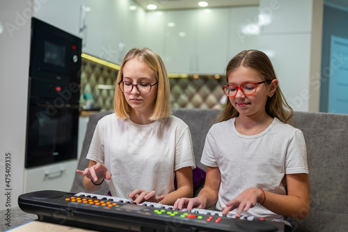 two teenage girls learning to play the piano at home.