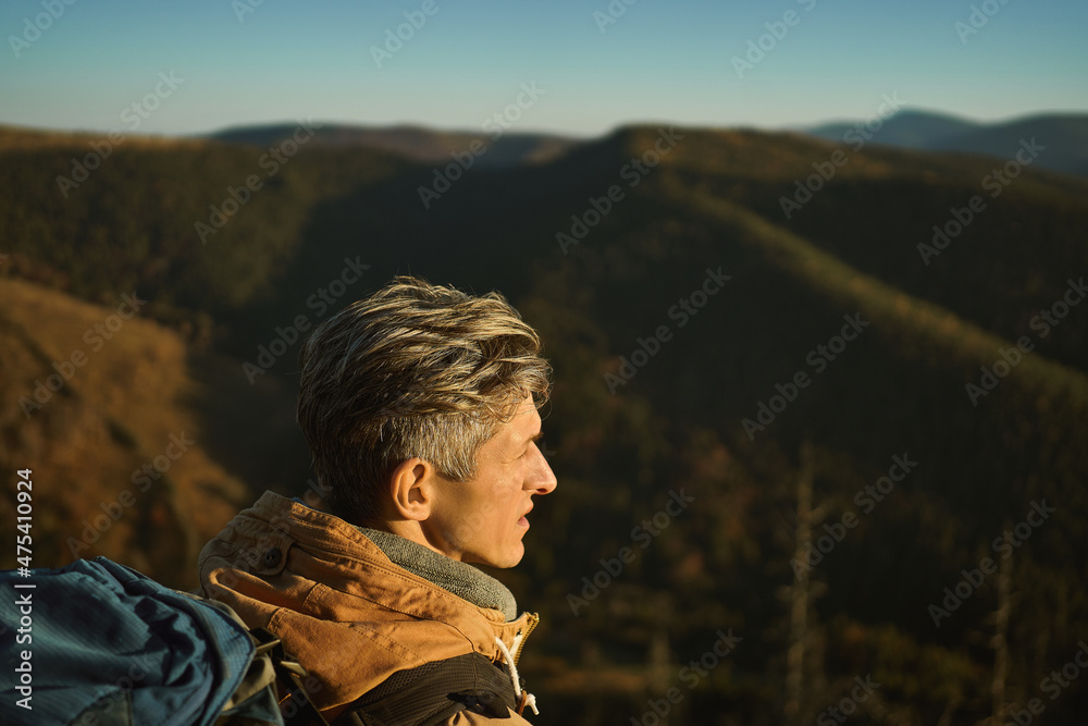 Close up face of tourist man looking confident and freedom with his hiking expedition outdoors on top of mountain at sunset.