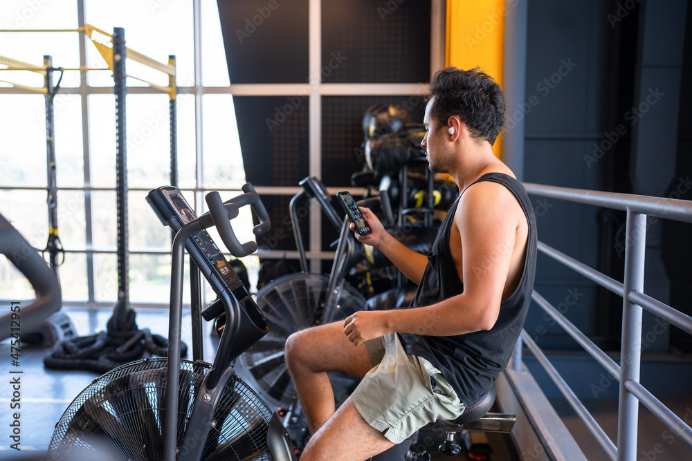Obraz premium Young man cheking his phone while he is on a cycling machine in the gym