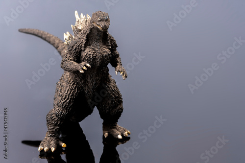 A black ugly looking lizard toy. Legendary Asian monster. A giant figure mascot. Plastic creature in detail on reflecting surface. Cultural object background with copy space. 