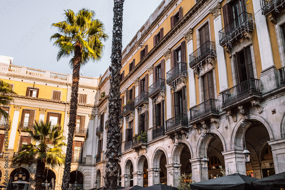 Apartment buildings on european square in old city. Windows with shutters, palm trees. Facade of pretty houses in south streets of Italy. Traveling, architecture concept.
