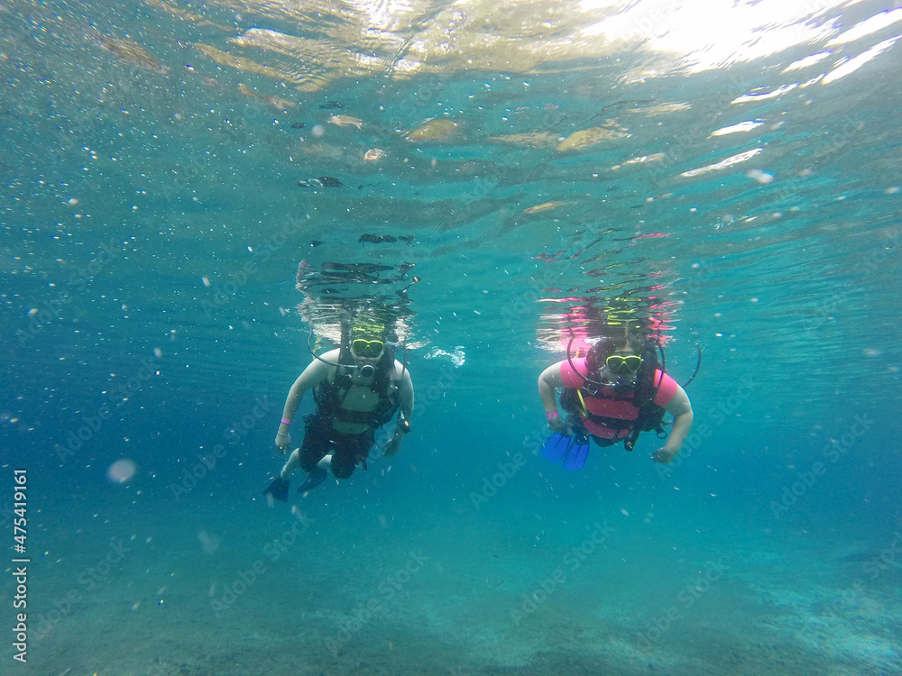 Couple scuba diving under crystal clear water with tank, fins and visor happy swim and share their love doing exercise and living a new experience
