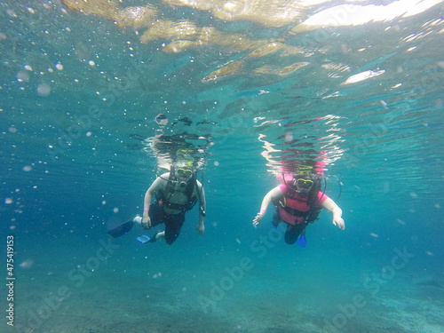 Couple scuba diving under crystal clear water with tank, fins and visor happy swim and share their love doing exercise and living a new experience 