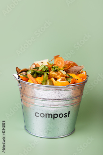 Sorted kitchen waste in compost-bucket on green background. Compost-container top view. Sustainable lifestyle. Vegetable, fruit peels, scraps from food preparation collected in trash-can for recycling