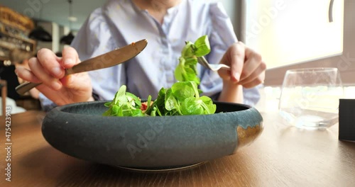 Front view of woman eating delicious bio organic vegan green salad in luxury restaurant from rustic plate
