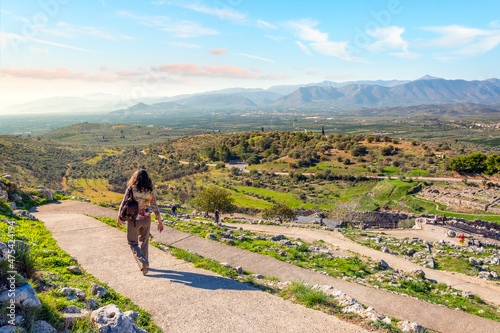 A female traveler walks down a path at the ancient Bronze age citadel of Mycenae, Greece with the Peloponnese area of Greece in view for miles. photo