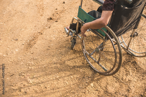 An anonymous paraplegic man on his old wheelchair with his hands resting on the handrims. Traveling on a dirt road. photo