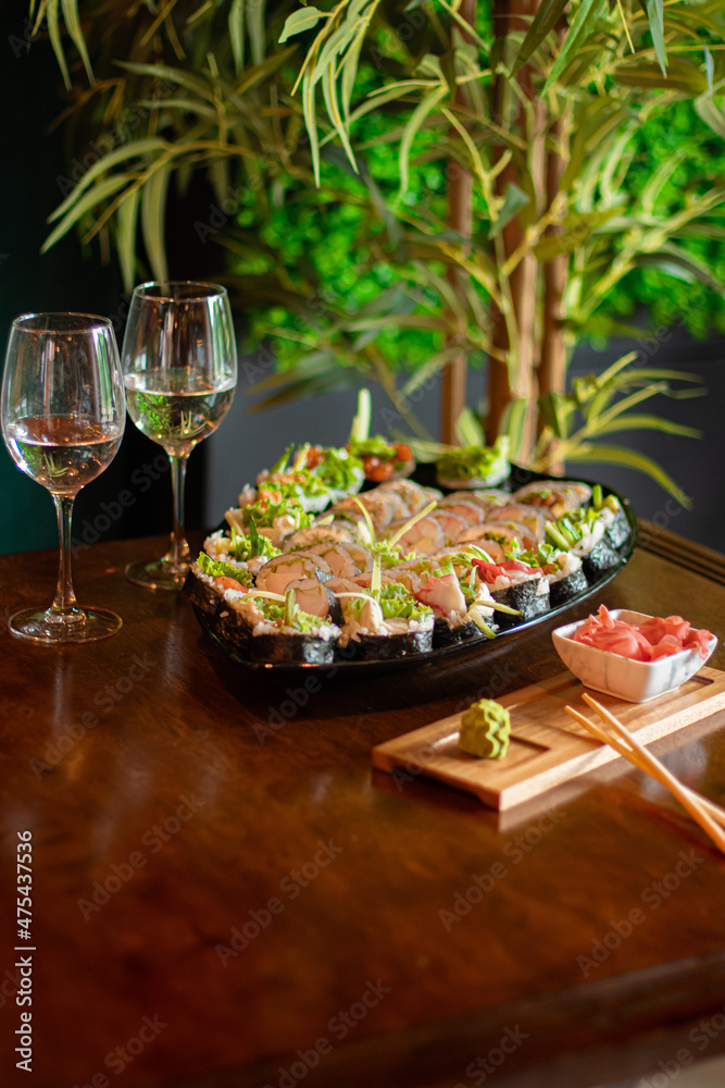 Φωτογραφία Sushi set na talerzu w restauracji z imbirem i wasabi, kieliszki wina, kolacja d