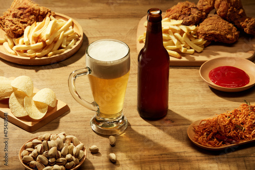 Fototapeta Naklejka Na Ścianę i Meble -  A glass and a bottle of beer with fried potatoes spicy chicken floss and fried chicken in brown background , mug of beer and food for advertising , front view 
