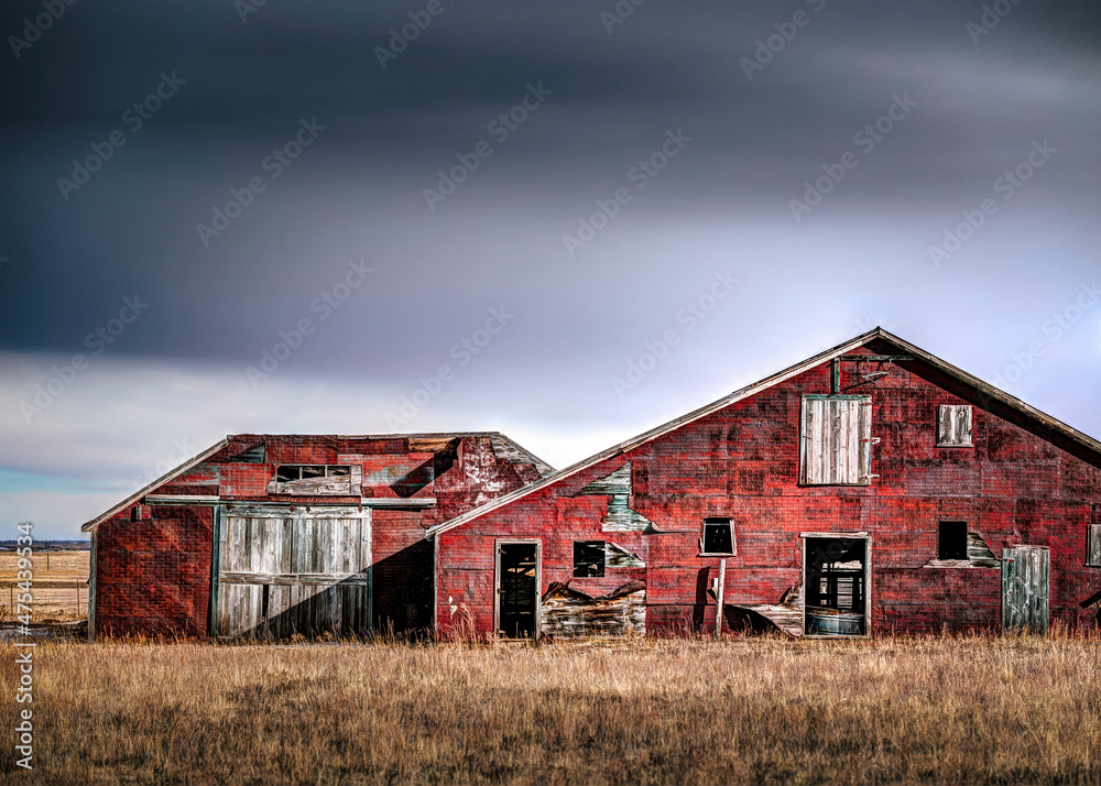 Old red spooky farmhouse in the countryside. The sky is dark and ominous. The doors and windows show a very dark interior.