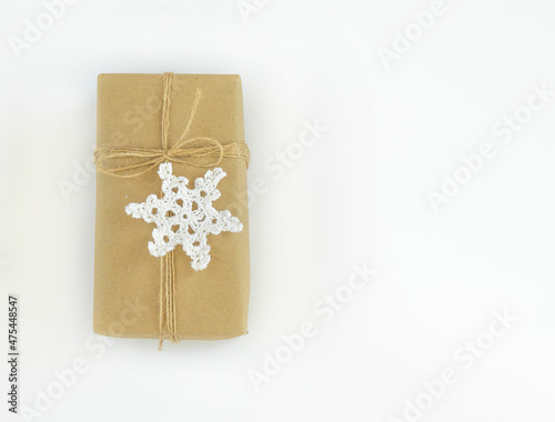 Christmas and New Years flatlay background. Gift box wrapped in kraft paper with jute cord. Decorated with a crocheted snowflake. Place for your text
