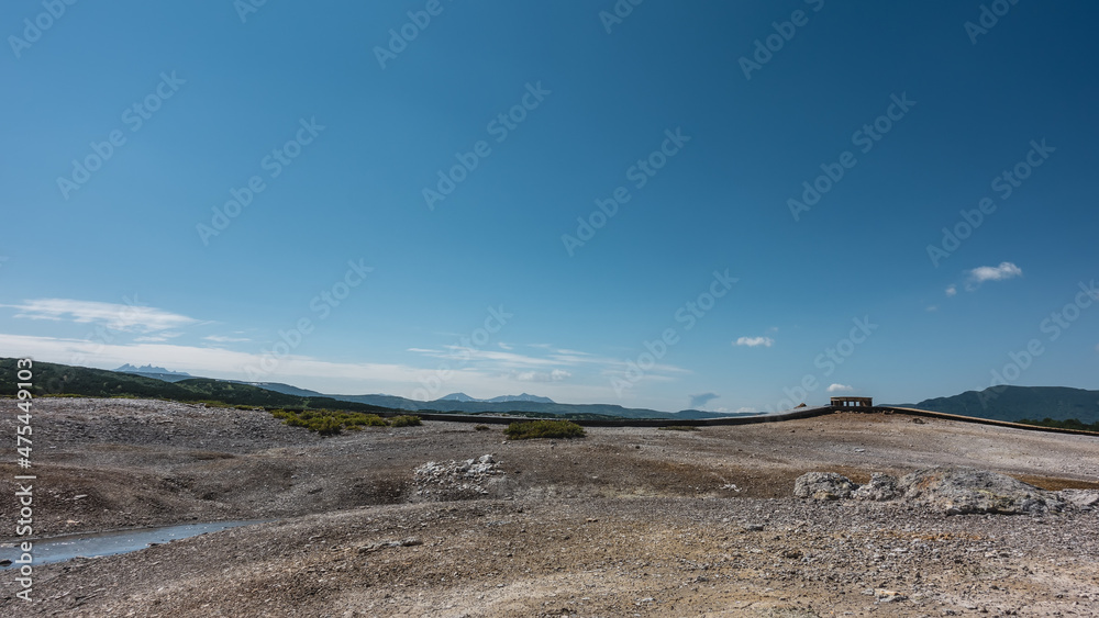 The rocky soil in the caldera of an extinct volcano is covered with sulfur deposits. Wooden paths for tourists are laid above the ground. Clear blue sky. Copy space. Kamchatka. Uzon The rocky soil in the caldera of an extinct volcano is covered with sulfur deposits. Wooden paths for tourists are laid above the ground. Clear blue sky. Copy space. Kamchatka. Uzon