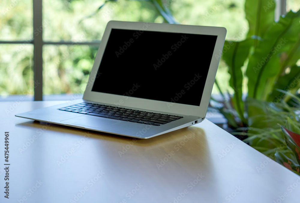 Black screen laptop computer on wooden table with greenery bokeh background. Black screen laptop computer on wooden table with greenery bokeh background.
