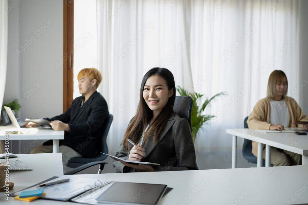 Confident businesswoman sitting with her colleagues in office and smiling to camera.
