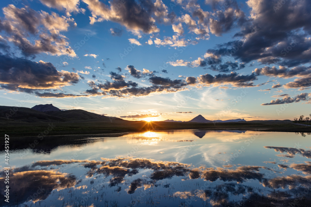 Sunset clouds reflect into wetlands along the Rocky Mountain Front with Haystack Butte near Augusta, Montana, USA