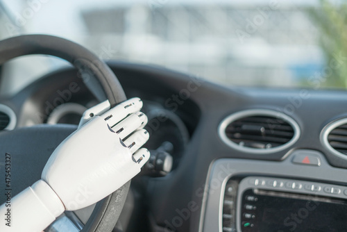 artificial robotic white arm holding steering wheel and driving vehicle