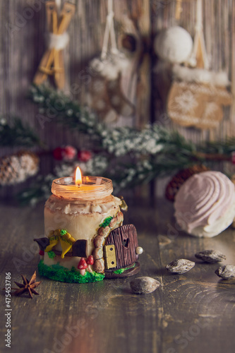 A burning handmade candle on the background of Christmas decor .
