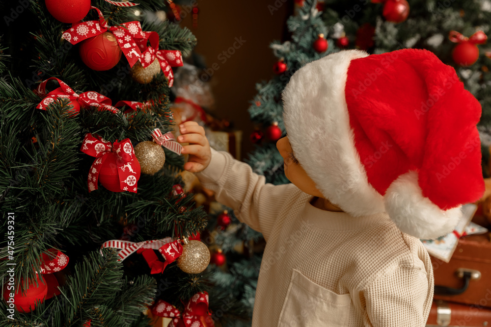 A child with Santa Clause hat helps to decorate Christmas tree
