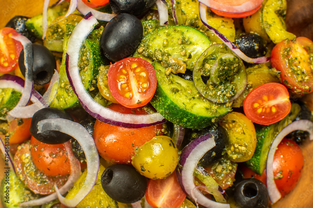 Healthy vegetable salad of fresh tomato, cucumber, onion, black olives,yellow sweet pepper with basil pesto sauce on wooden bowl.Top view, copy space. 