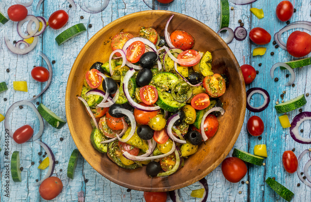 Healthy vegetable salad of fresh tomato, cucumber, onion, black olives,yellow sweet pepper with basil pesto sauce on wooden bowl.Top view, copy space. Healthy vegetable salad of fresh tomato, cucumber, onion, black olives,yellow sweet pepper with basil pesto sauce on wooden bowl.Top view, copy space.