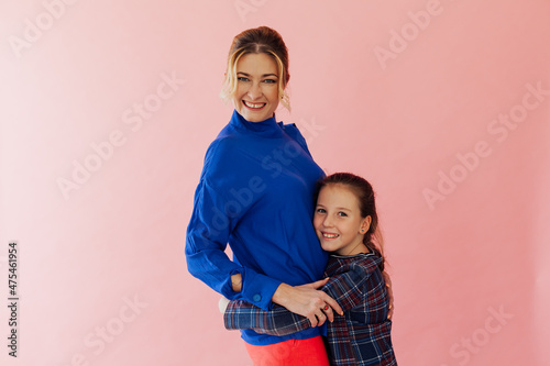 mother and daughter embrace smiling against a pink background