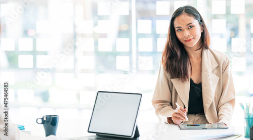 Portrait of beautiful businesswoman using digital tablet at office, smiling and looking at camera