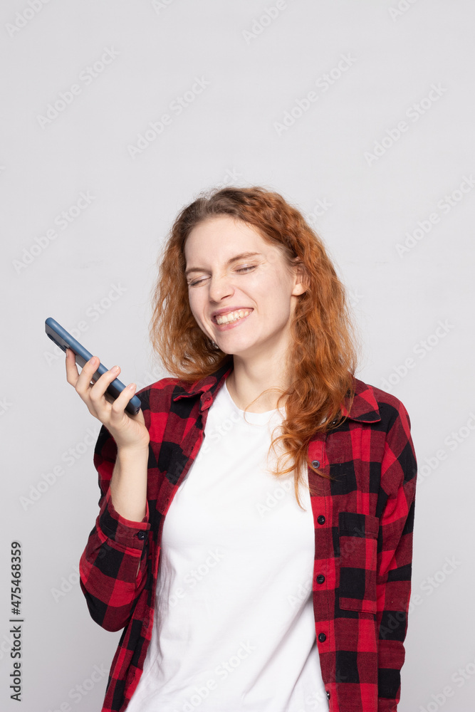 Fototapeta premium girl in a plaid shirt on a light background with a smartphone
