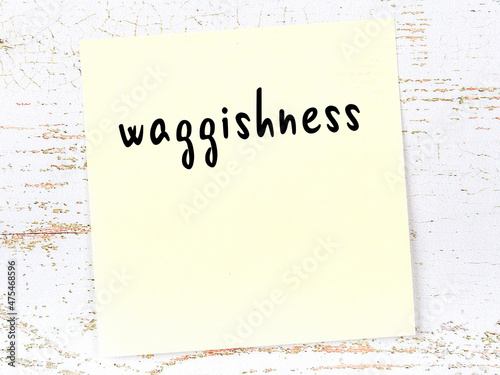 Yellow sticky note on wooden wall with handwritten word waggishness photo