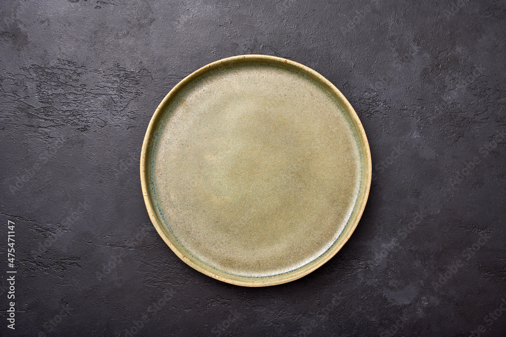 Empty green rustic ceramic plate with black rim on a light textured graphite background, flat lay, copy space Empty green rustic ceramic plate with black rim on a light textured graphite background, flat lay, copy space