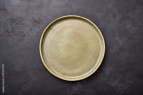Empty green rustic ceramic plate with black rim on a light textured graphite background, flat lay, copy space