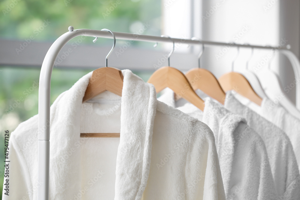 Rack with white bathrobes in room, closeup Rack with white bathrobes in room, closeup
