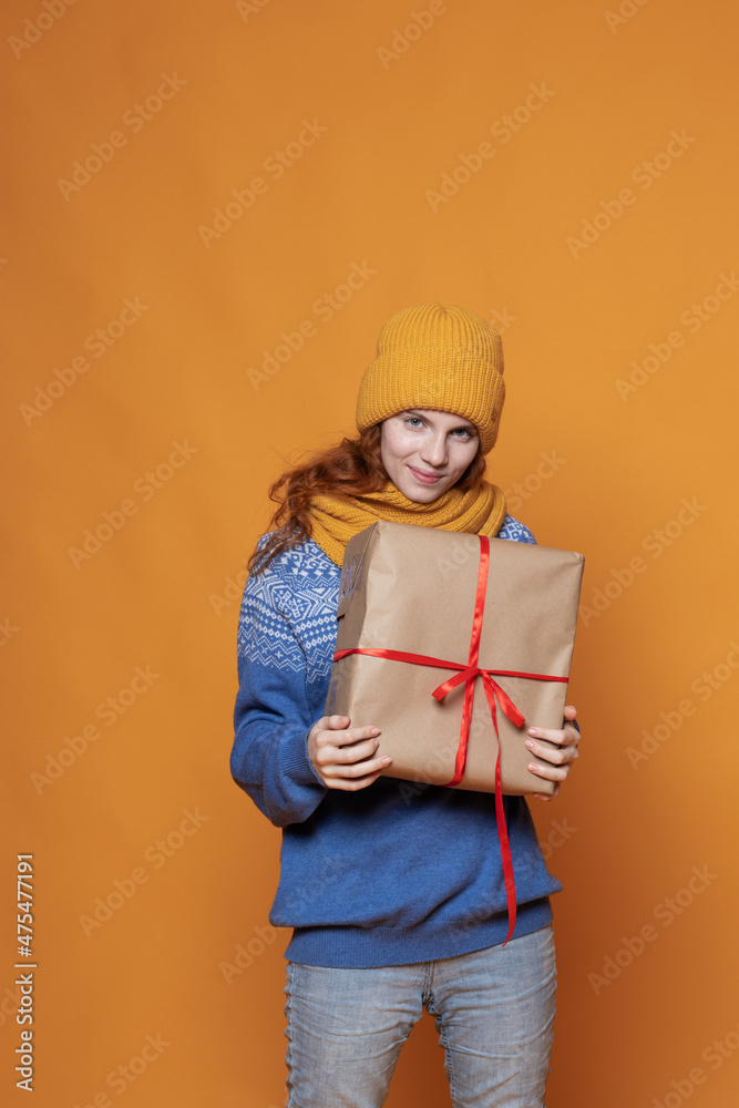 young girl in a warm hat and sweater is holding a gift on a yellow background