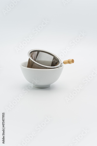 metal tea strainer in a white stoneware bowl on a white tabletop photo
