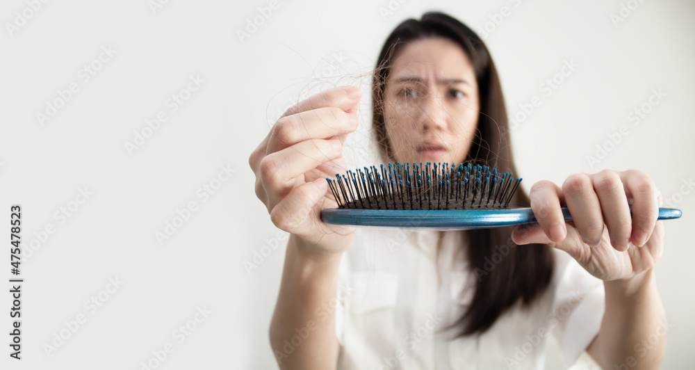 Asian woman are looking hair loss and use hand remove hair from comb with worried and unhappy