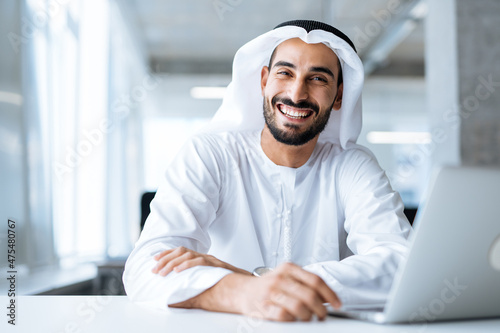 Handsome man with dish dasha working in his business office of Dubai. Portraits of a successful businessman in traditional emirates white dress. Concept about middle eastern cultures
