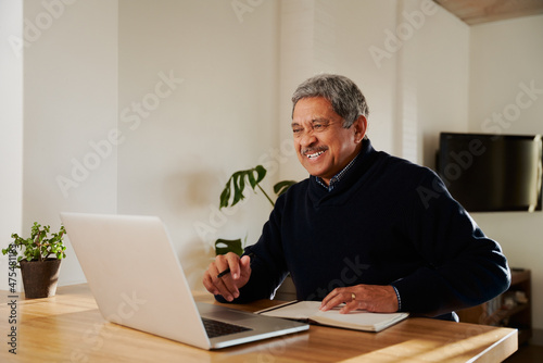 Multi-cultural elderly male smiling while on online call with family. Isolating in modern home, sitting at kitchen counter.