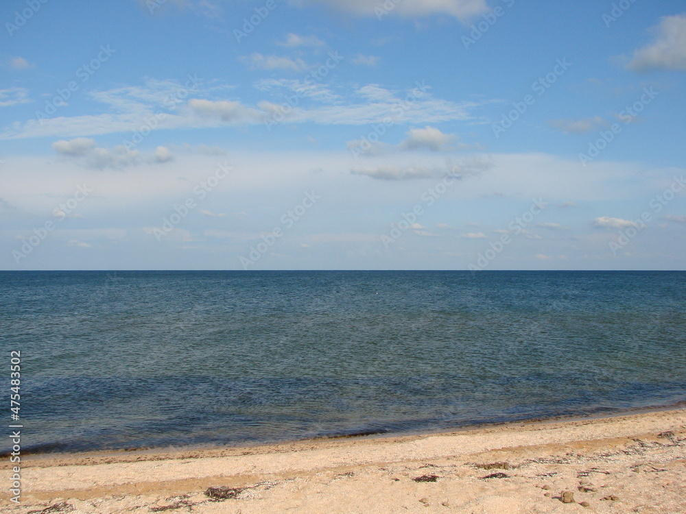 Panorama of the sandy beach near the crystal clear waters of the calm sea on a background of barely cloudy evening sky.