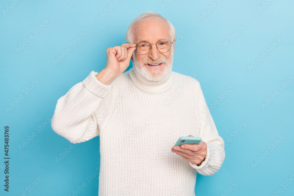 Photo of nice elder beard man hold telephone wear eyewear white turtleneck isolated on blue color background Photo of nice elder beard man hold telephone wear eyewear white turtleneck isolated on blue color background