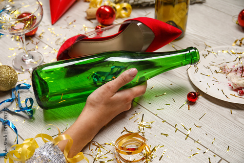Wall Mural Drunk young woman with empty bottle of wine lying on floor after party