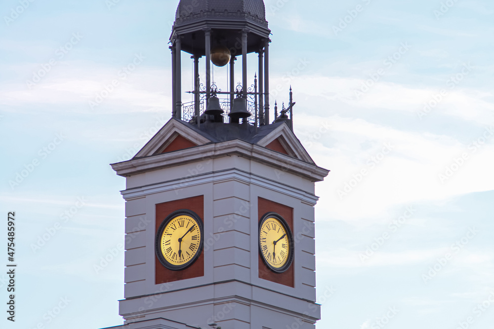Reloj en la torre del edificio principal de la plaza Puerta del Sol. Reloj con sus manecillas iluminadas al atardecer en el palacio de Correos, actual presidencia de la Comunidad de Madrid, España.