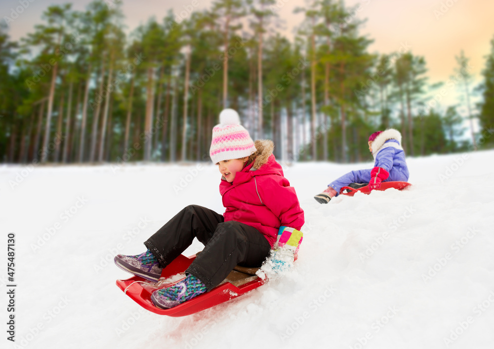 childhood, sledging and season concept - happy little girl sliding down on sled outdoors in winter over snowy park or forest background childhood, sledging and season concept - happy little girl sliding down on sled outdoors in winter over snowy park or forest background