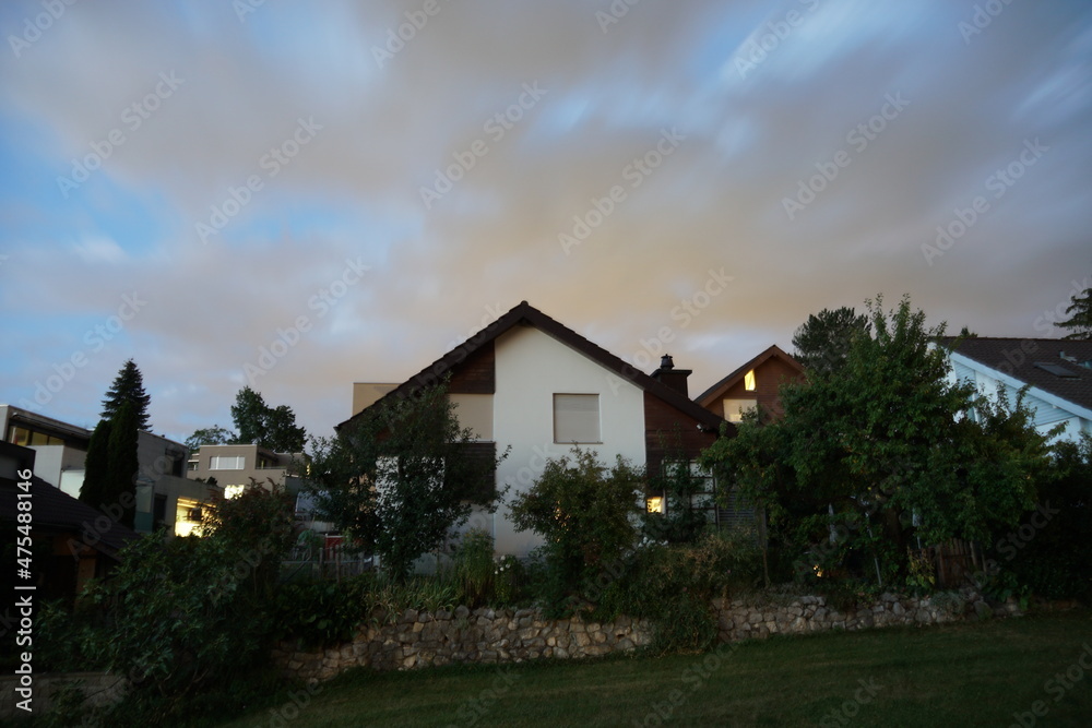 Typical family houses with lights in windows in Switzerland countryside in canton Zurich with gardens full of green vegetables and fruit trees during sunset under overcast sky.