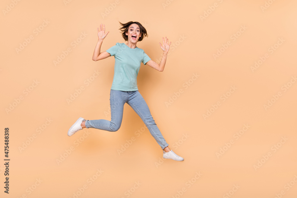 Full length photo of young girl have fun jump up wave hi friendly travle dream isolated over beige color background