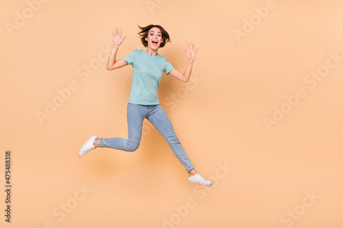 Full length photo of young girl have fun jump up wave hi friendly travle dream isolated over beige color background photo