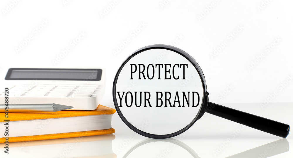 Magnifier with text ROTECT YOUR BRAND with notebook, calculator on the white background Magnifier with text ROTECT YOUR BRAND with notebook, calculator on the white background