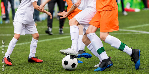 Background image of football game. Legs of soccer players kicking vlack and white soccer ball on artificial grass pitch. Soccer coach on sideline photo