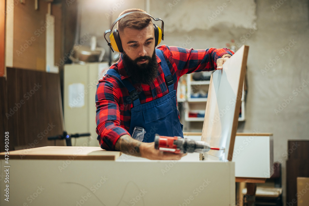 Young male carpenter working in workshop while using power drill Young male carpenter working in workshop while using power drill