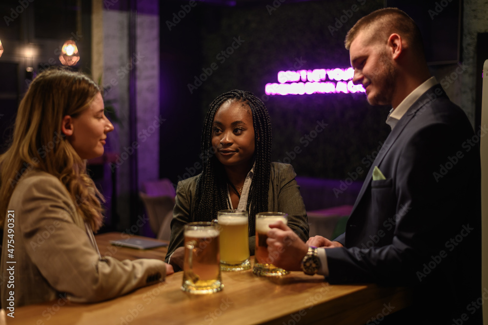 Cheerful colleagues drinking beer in the bar together after work and using a tablet