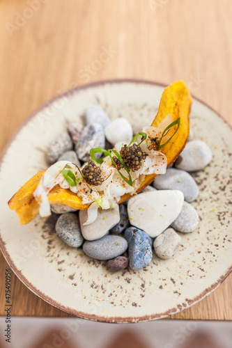 Top view closeup of seafood canape ready to eat on the table. Banana chifles with fake squid noodles and beluga caviar on wooden table served for lunch. Luxurious delicatessen food.