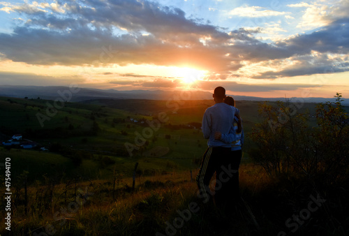 A young couple climbing a hill watching the beautiful sunset and landscape in the distance